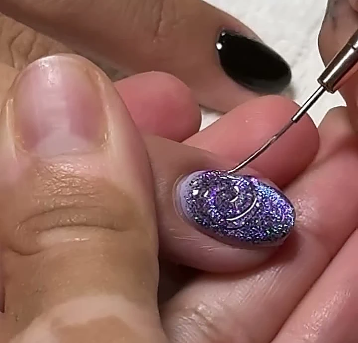 Manicurista trazando una espiral fina sobre una uña con glitter lila