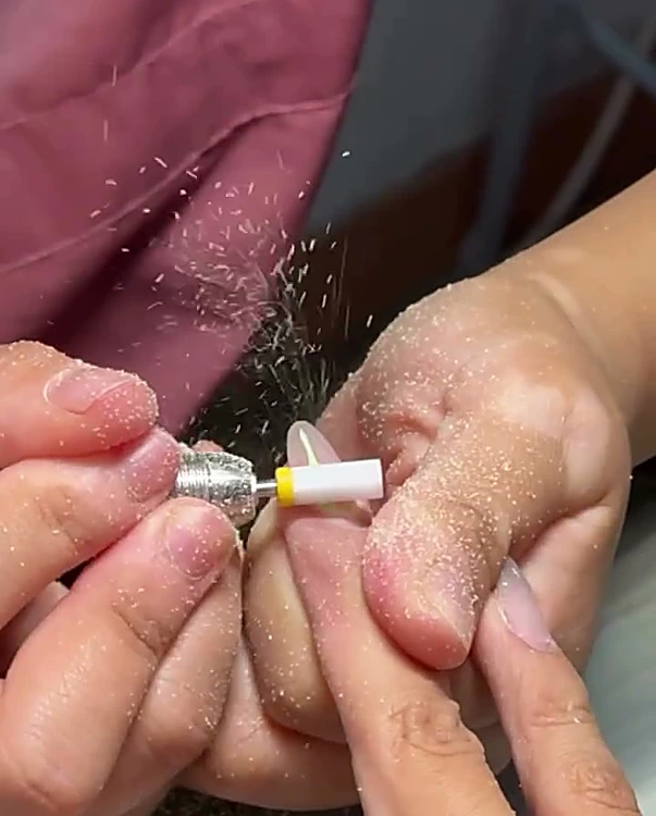 Manicurista con guantes limando y nivelando una uña con torno eléctrico