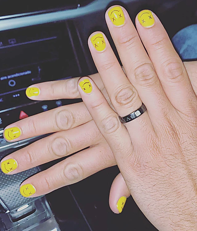 Mano de hombre con uñas cortas pintadas de amarillo con caritas